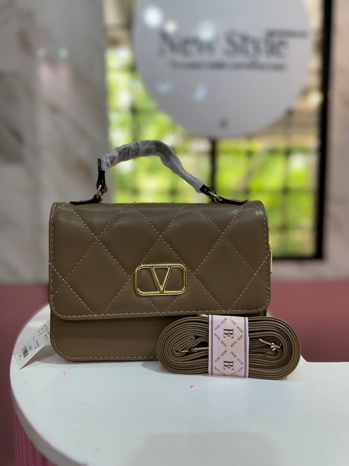 Cartera de mano en color café con acabado acolchado y correa ajustable a juego
