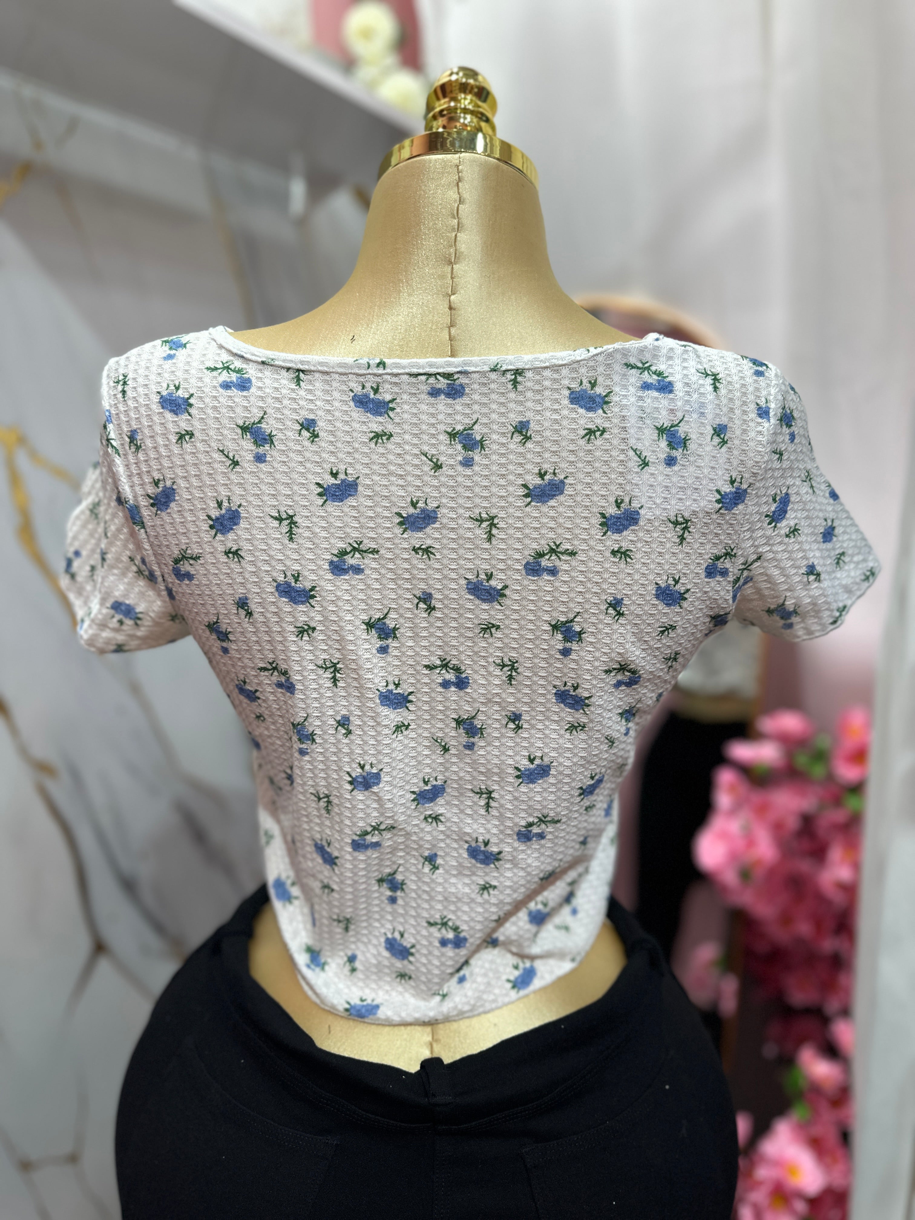 Crop top blanco con estampado floral azul y diseño de botones enfrente
