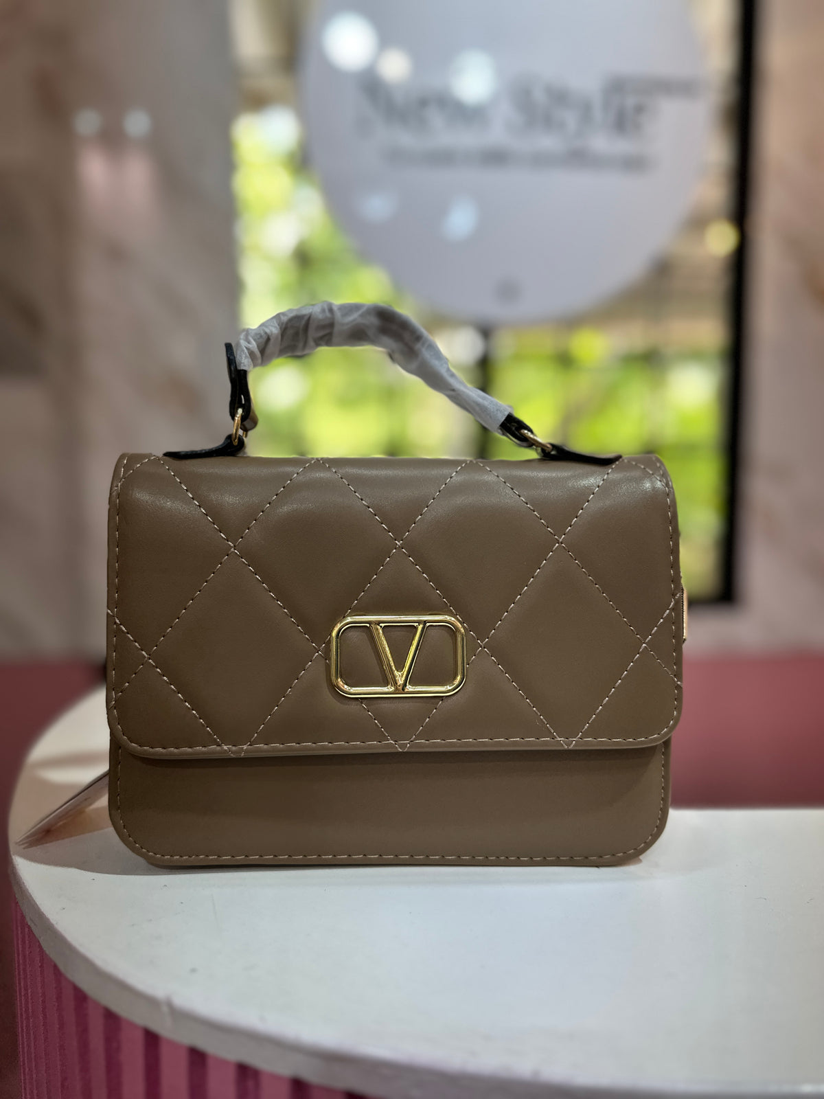 Cartera de mano en color café con acabado acolchado y correa ajustable a juego