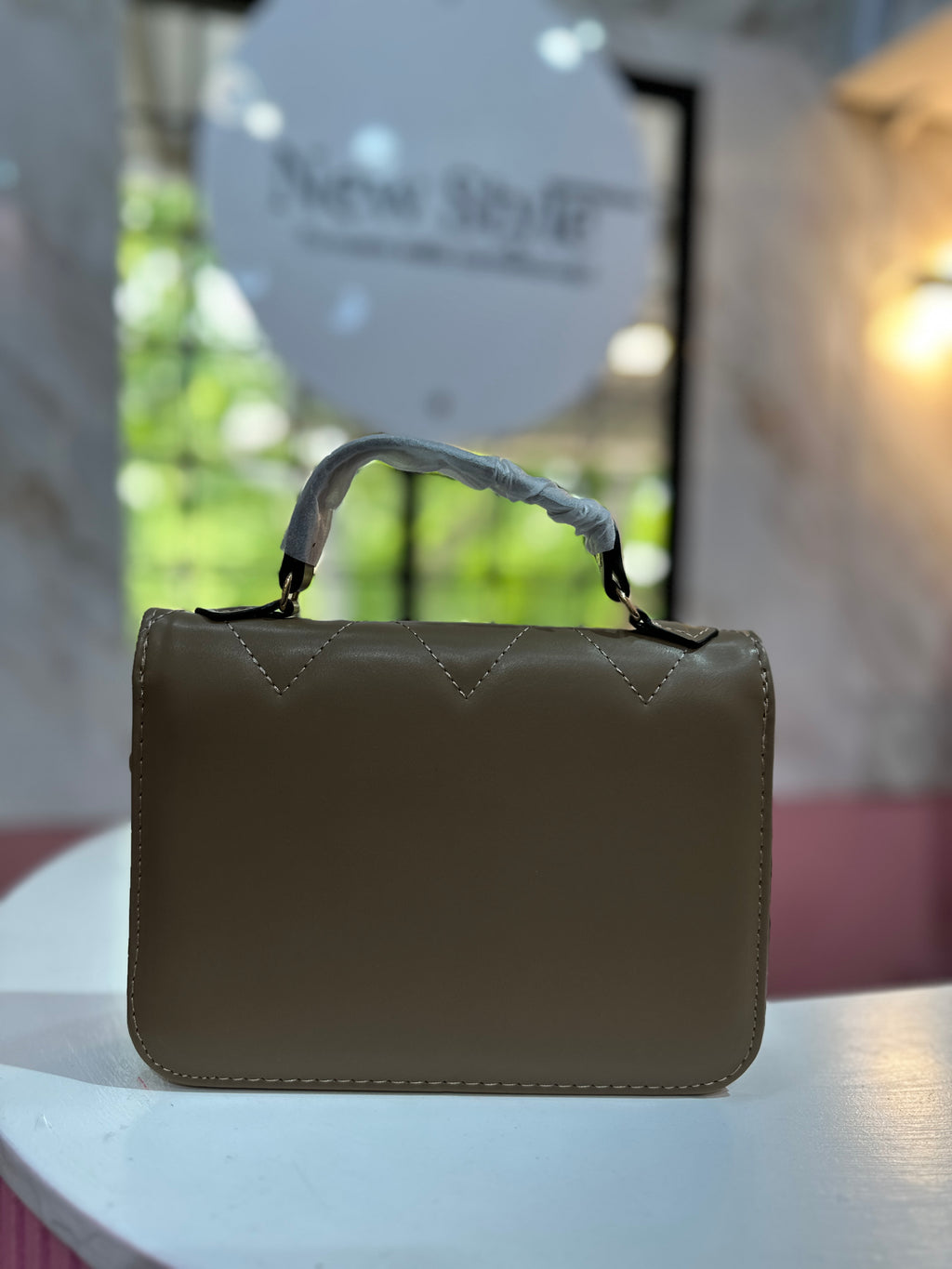 Cartera de mano en color café con acabado acolchado y correa ajustable a juego